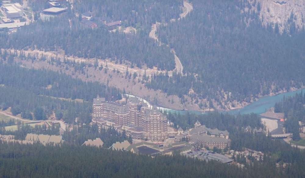 Aerial view of a large, castle-like hotel surrounded by a forest with a winding river nearby, reminiscent of the enchanting gondolas in Banff.