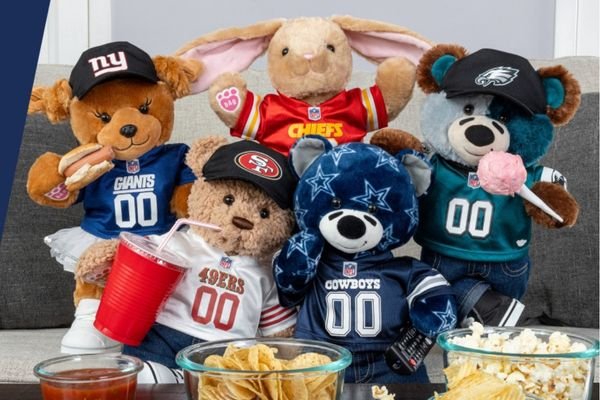 Five stuffed animals wearing different NFL team jerseys and hats are arranged together on a couch at the West Edmonton Mall Attractions. Various snacks, including chips and dip, are placed in front of them.