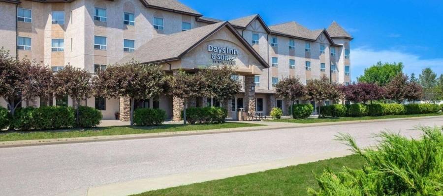 Four-story Days Inn & Suites hotel with beige exterior, stone accents, and trees in front under a clear blue sky, conveniently located among hotels near West Edmonton Mall.