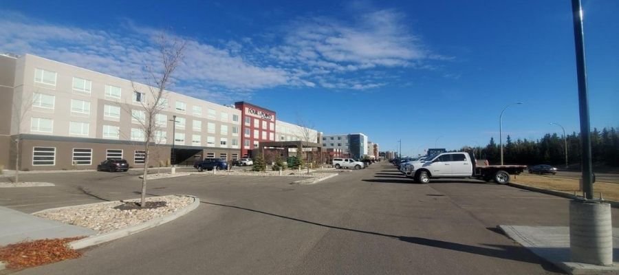 A parking lot outside a modern hotel complex near West Edmonton Mall, with several parked cars and a clear blue sky in the background.