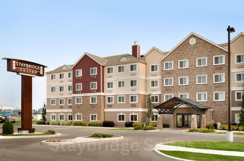 Front view of Staybridge Suites hotel with a large sign to the left and an entrance with a covered driveway. This four-story building, featuring a mix of beige and red facade, is one of the top hotels near West Edmonton Mall.