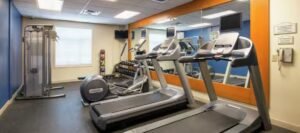 A small gym equipped with two treadmills, a cable machine, free weights, medicine balls, and a large mirror on the wall is perfect for guests staying at hotels near West Edmonton Mall.