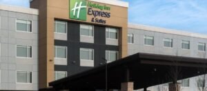 Front view of a Holiday Inn Express & Suites hotel building with a modern design featuring a black and beige exterior. Located conveniently among hotels near West Edmonton Mall, the property boasts multiple windows and a large entrance canopy.