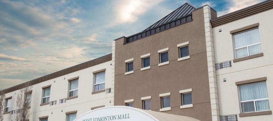 The image shows the exterior of the West Edmonton Mall Inn, a three-story building with beige walls and several windows. The entrance canopy reads “West Edmonton Mall Inn”. It's one of the convenient hotels near West Edmonton Mall, making it a great choice for travelers.