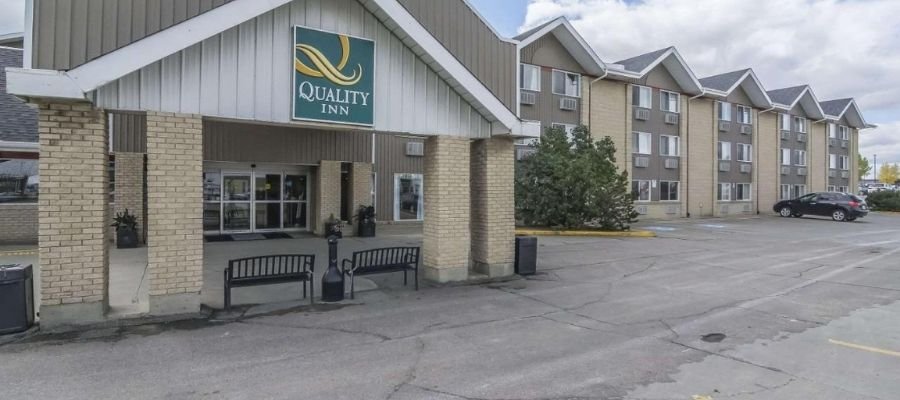 The exterior view of a Quality Inn hotel, conveniently located near West Edmonton Mall, showcases a multi-story building with a covered entrance and a few parked cars.