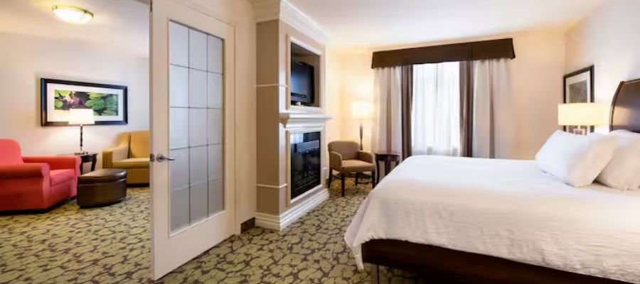 Hotel room with a large bed, an armchair, and a flatscreen TV. This stylish space also features a cozy seating area with an armchair, loveseat, and side table. The decor includes framed art on the wall. Ideal for guests looking for comfortable hotels near West Edmonton Mall.