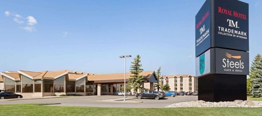 A two-story hotel building with a large sign in the foreground displaying the names "Royal Hotel," "TM Trademark Collection by Wyndham," and "Steels Cafe & Grill," is among the esteemed hotels near West Edmonton Mall.