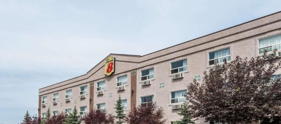 A three-story Super 8 motel near West Edmonton Mall features air conditioning units visible under each window, surrounded by trees and shrubs.