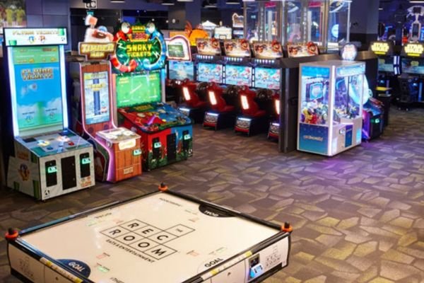 The Rec Room arcade at West Edmonton Mall Attractions features various gaming machines, including claw machines, arcade cabinets, and an air hockey table. The floor is adorned with a geometric patterned carpet.