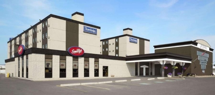 Exterior view of a multi-story hotel building with "Travelodge" and "Smitty's" signs. The building has a beige and brown color scheme, with a flat roof and an adjacent entrance area with columns, typical of hotels near West Edmonton Mall.