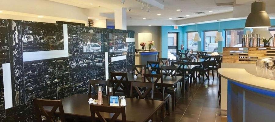 An interior view of an empty café with dark wooden chairs and tables, a marble partial divider, modern light fixtures, and bright blue walls—reminiscent of lounges in hotels near West Edmonton Mall.