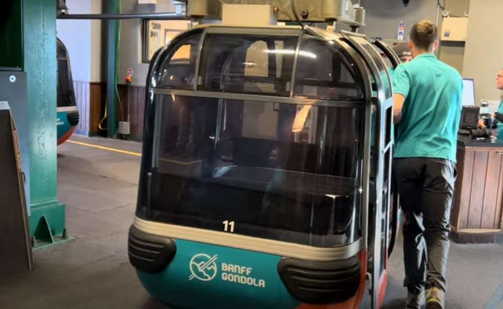 A worker in a green uniform checks a stationary Banff Gondola cabin, marked with the number 11, inside a station. These gondolas in Banff offer breathtaking views and reliable service for all visitors.