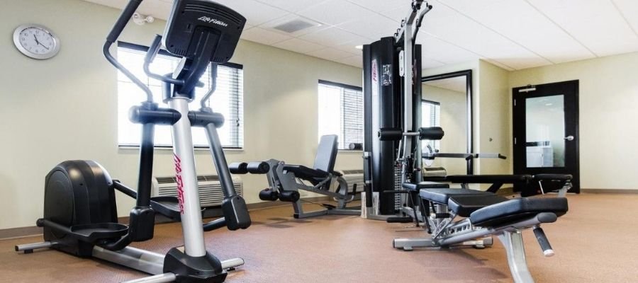 A well-lit gym in hotels near West Edmonton Mall, featuring cardio and strength training equipment, including an elliptical machine, weight bench, and multi-exercise machine.