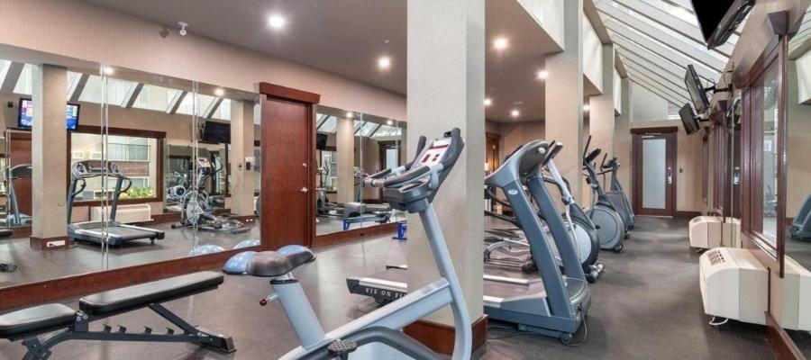 A gym with various exercise equipment including treadmills, a bench, and weight machines. There are mirrors on the walls and natural light streaming in from skylights above, offering a perfect spot for travelers staying at hotels near West Edmonton Mall to maintain their fitness routine.