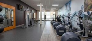 A well-lit gym room with treadmills, stationary bikes, and weight machines. A large mirror and exercise balls are on the left, while a mural of outdoor scenery decorates one wall. Perfect for guests of hotels near West Edmonton Mall seeking a fitness break.