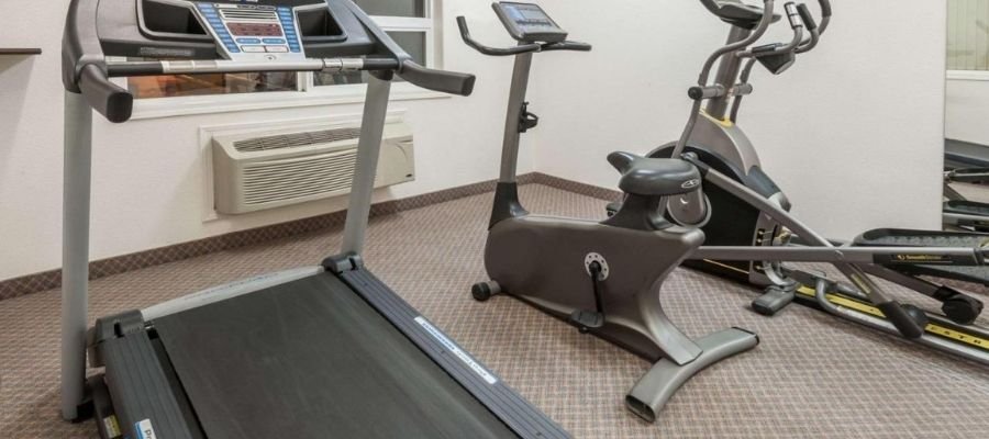 A small fitness room in hotels near West Edmonton Mall features a treadmill, exercise bike, and elliptical machine on a carpeted floor.