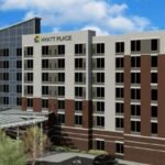 Exterior view of the Hyatt Place hotel building under a blue sky with greenery and landscaping in the foreground, conveniently situated among hotels near West Edmonton Mall.