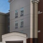 Exterior view of a Candlewood Suites hotel building with a beige and brown facade, several windows, and brand signage under a clear sky. Ideal for travelers looking for hotels near West Edmonton Mall.