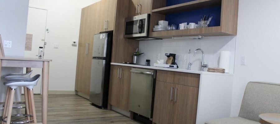 Modern kitchen with wooden cabinets, stainless steel appliances, a sink, and a small dining area with stools. Ideal for guests visiting hotels near West Edmonton Mall.