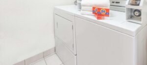 A white washer and dryer set in a laundry room with a box of Tide detergent and folded towels on top, reminiscent of the convenience you would find in hotels near West Edmonton Mall.