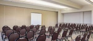 An empty conference room is set up with rows of chairs facing a projector screen and a blank wall. The room, often found in hotels near West Edmonton Mall, has a beige color scheme and fluorescent lighting.