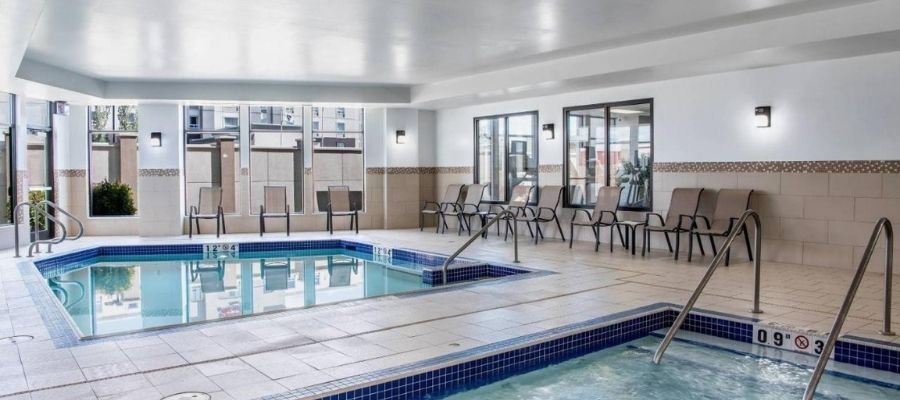 Indoor swimming pool area at hotels near West Edmonton Mall, featuring a hot tub, with chairs and tables arranged along the walls and windows providing natural light.