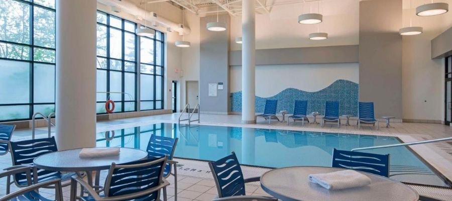 An indoor swimming pool with several lounge chairs, tables with towels, and large windows letting in natural light is one of the many luxurious amenities you’ll find at hotels near West Edmonton Mall.
