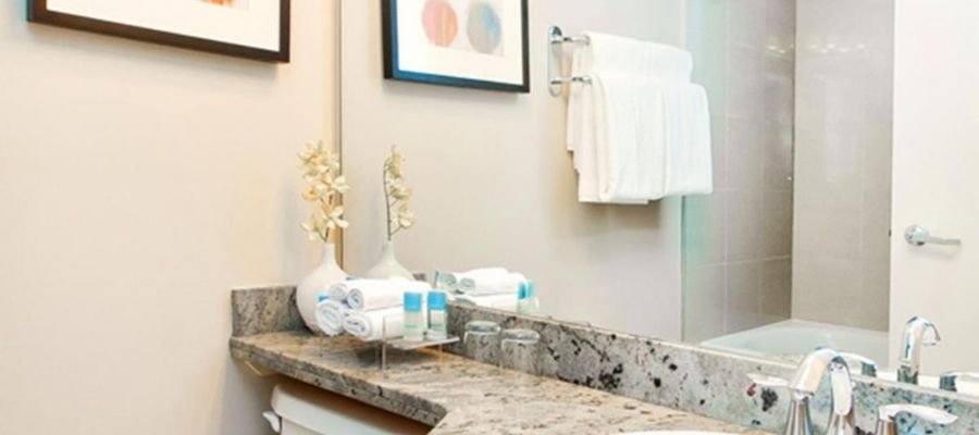 A bathroom with a granite countertop, a large mirror, towels, toiletries, and framed art on the wall. Just like the refined amenities you'd find in hotels near West Edmonton Mall.
