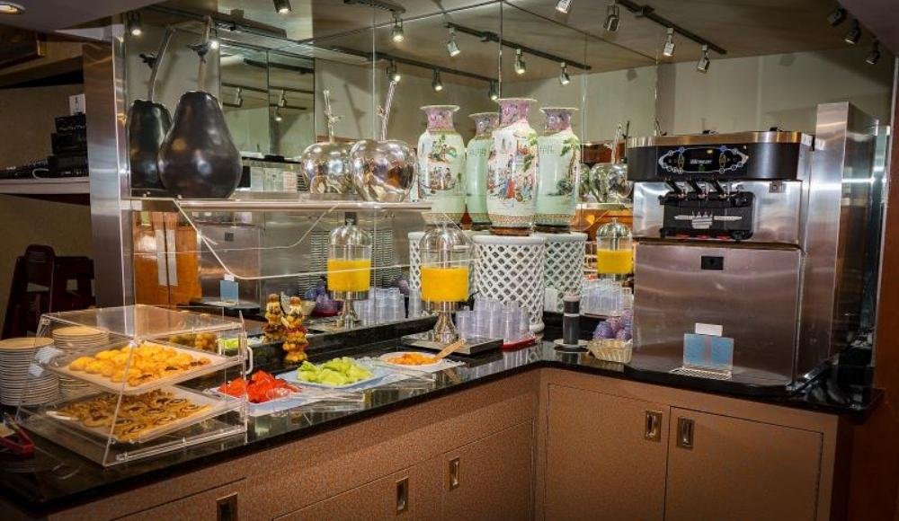 Discover the delightful buffet setup reminiscent of the finest buffets in Edmonton, featuring elegant vases, refreshing juice dispensers, a sleek coffee machine, and trays brimming with pastries and fresh fruit on a beautifully prepared countertop.