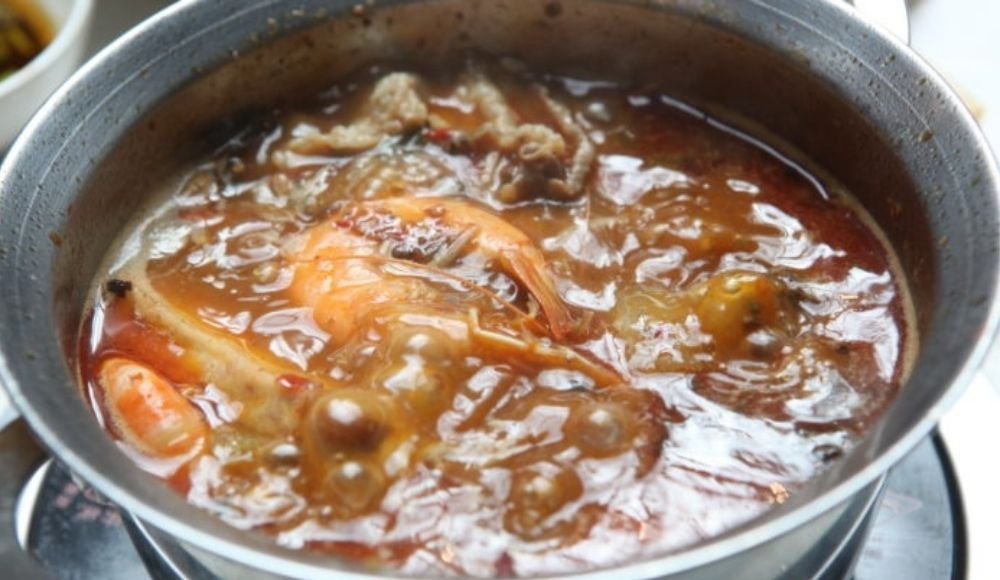 A pot of simmering soup with shrimp and various meats in a rich, brown broth, reminiscent of the hearty selections you might find at buffets in Edmonton.