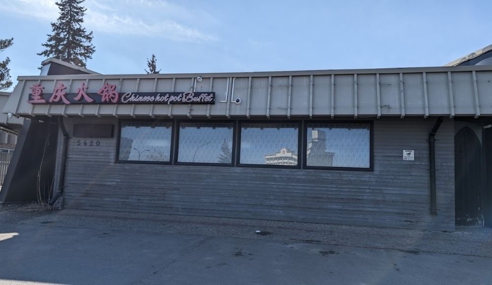 Exterior of Chongqing hot pot buffet restaurant, reminiscent of popular buffets in Edmonton, featuring closed windows and a gray facade with trees gently swaying in the background.