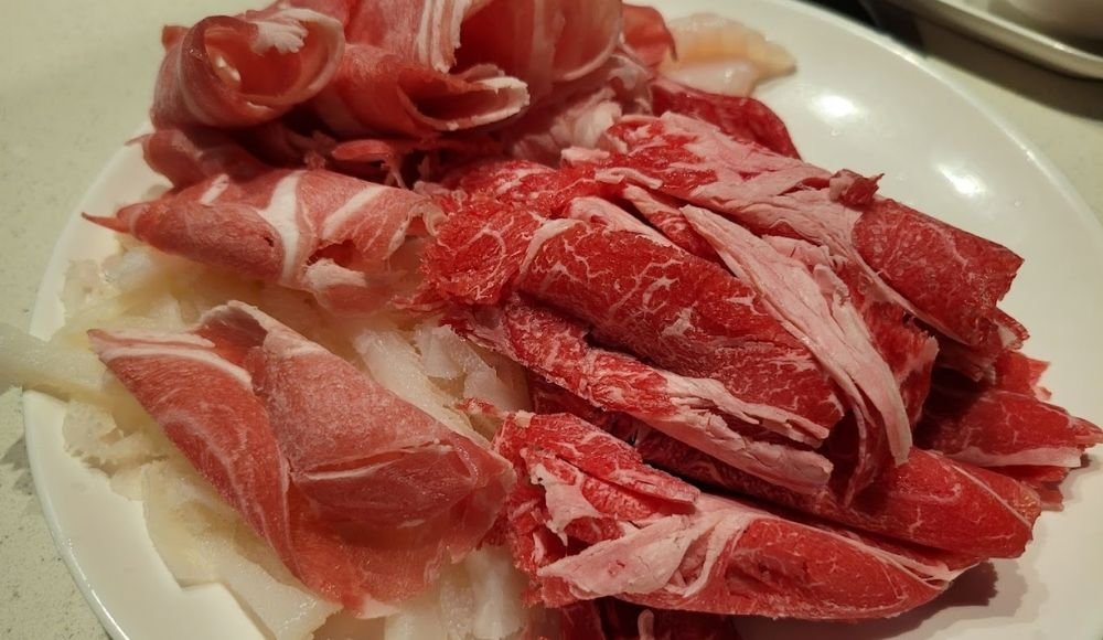 A plate with assorted uncooked sliced meats, including darker red and lighter pink varieties, perfect for those exploring buffets in Edmonton.