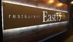 Sign for East75 restaurant and lounge on a wooden wall background, featuring a modern design and illuminated lettering. Known for offering one of the best buffets in Edmonton, it’s a spot where style meets delectable dining experiences.