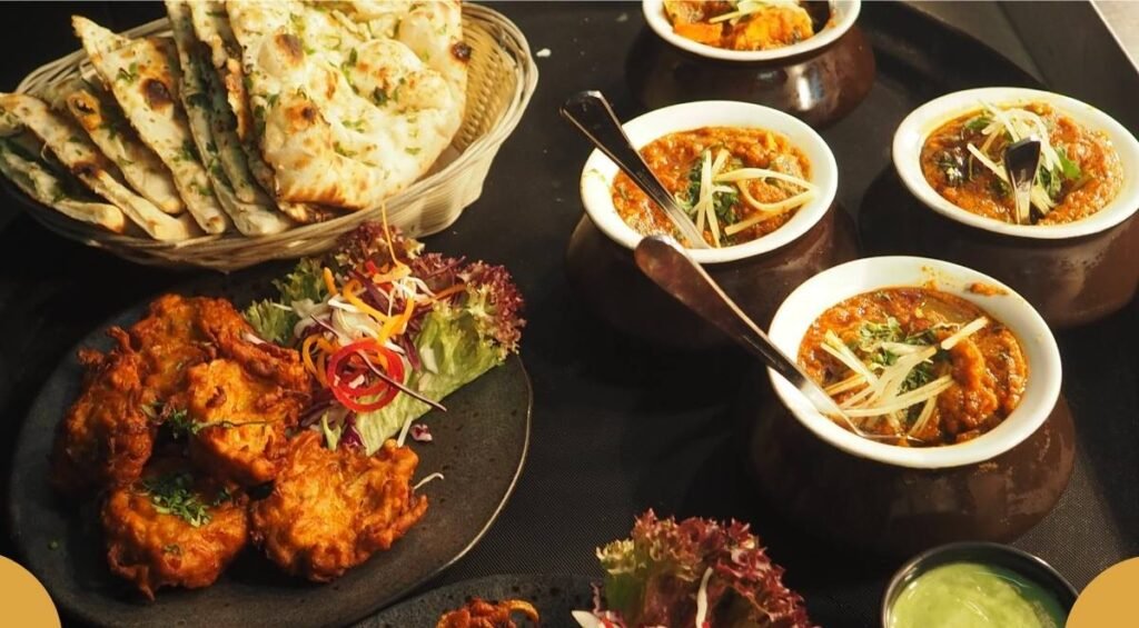 A spread of Indian food from one of the best restaurants in Banff includes naan, curry in pots, and pakoras on a plate, all garnished with herbs and vegetables.