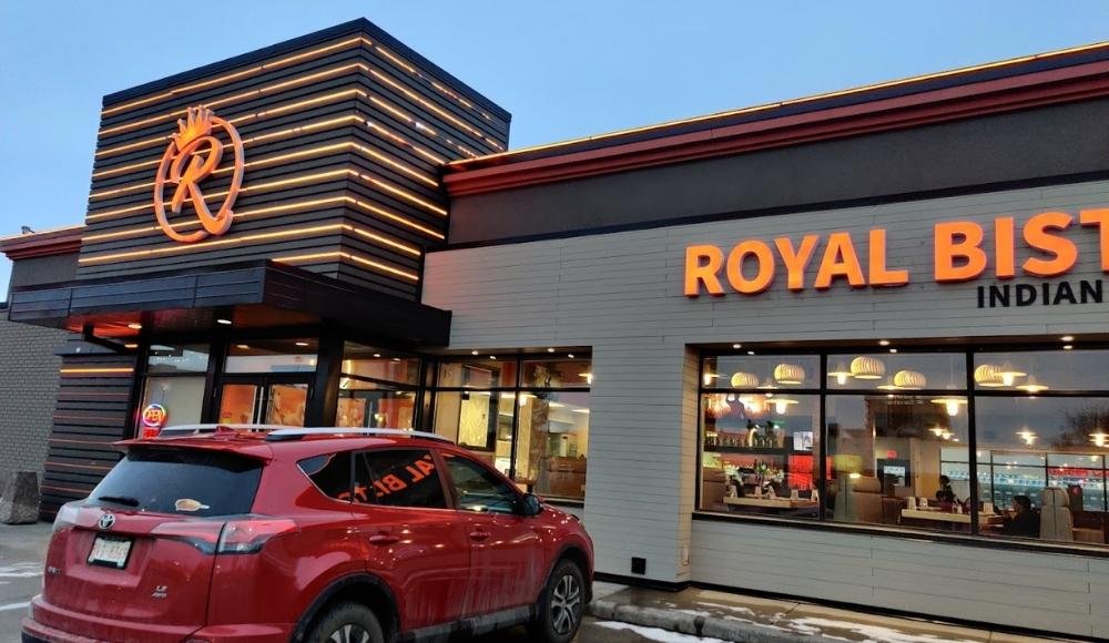 A red SUV is parked in front of Royal Bistro, an Indian restaurant known for its modern signage and large windows. Famous among those seeking buffets in Edmonton, it offers a delightful spread that draws food enthusiasts from all over the city.