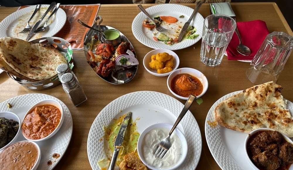 A wooden table set for a feast showcases an array of Indian dishes, featuring naan, curry, salad, sauces, and utensils, reminiscent of buffets in Edmonton.