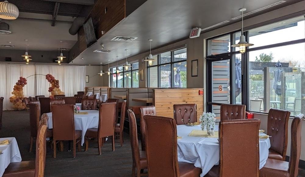 A restaurant interior with brown leather chairs, white tablecloths, and large windows creates an inviting atmosphere. Balloon decorations near a doorway hint at celebration, similar to the festive vibe of buffets in Edmonton.