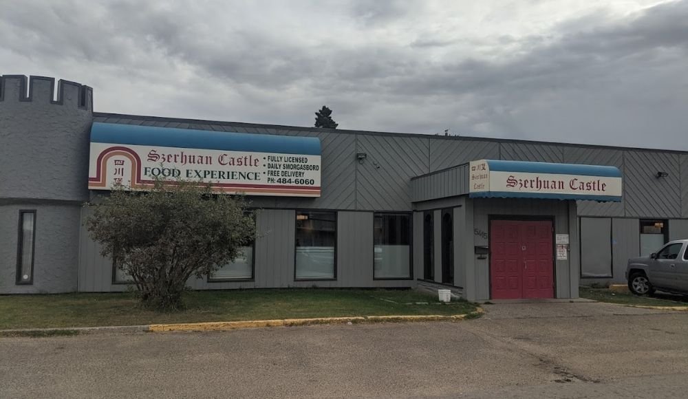 The exterior of a building displays signs reading "Szechan Castle Food Experience," offering a tantalizing glance into one of the finest buffets in Edmonton. It features a gray facade, bold red doors, and a parked truck on the right.