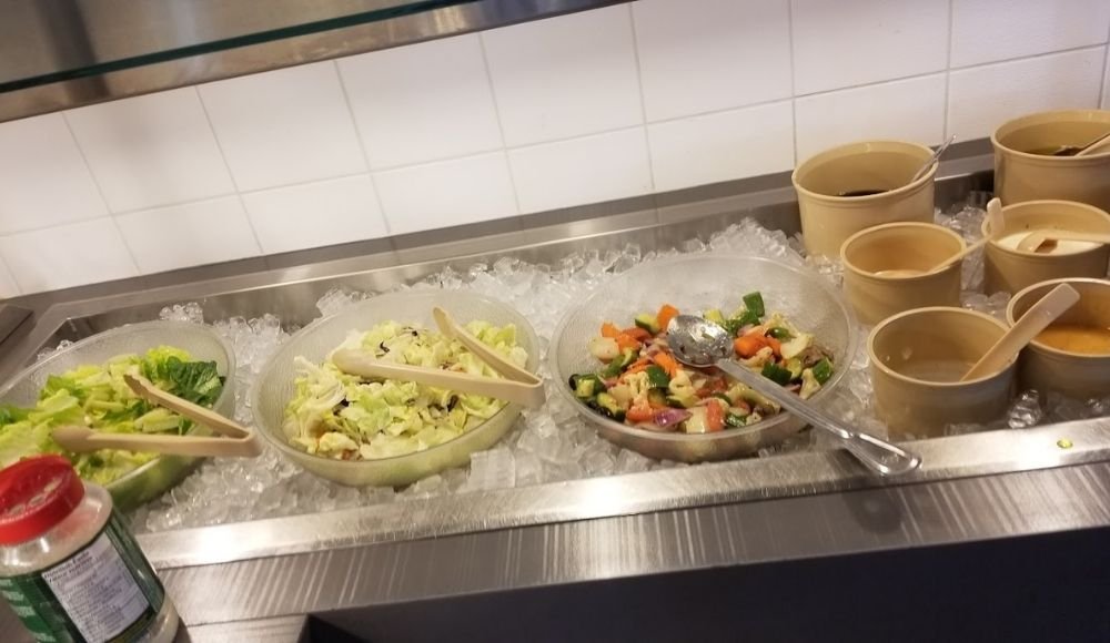 Discover our salad bar, a standout among buffets in Edmonton, featuring bowls of leafy greens, mixed vegetables, and various dressings, all set on ice.