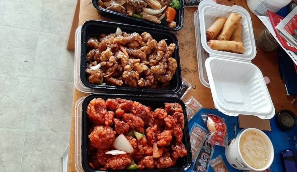 A delightful medley of takeout food containers showcases fried chicken, egg rolls, and stir-fried vegetables on a table—offering a taste reminiscent of the best buffets in Edmonton.