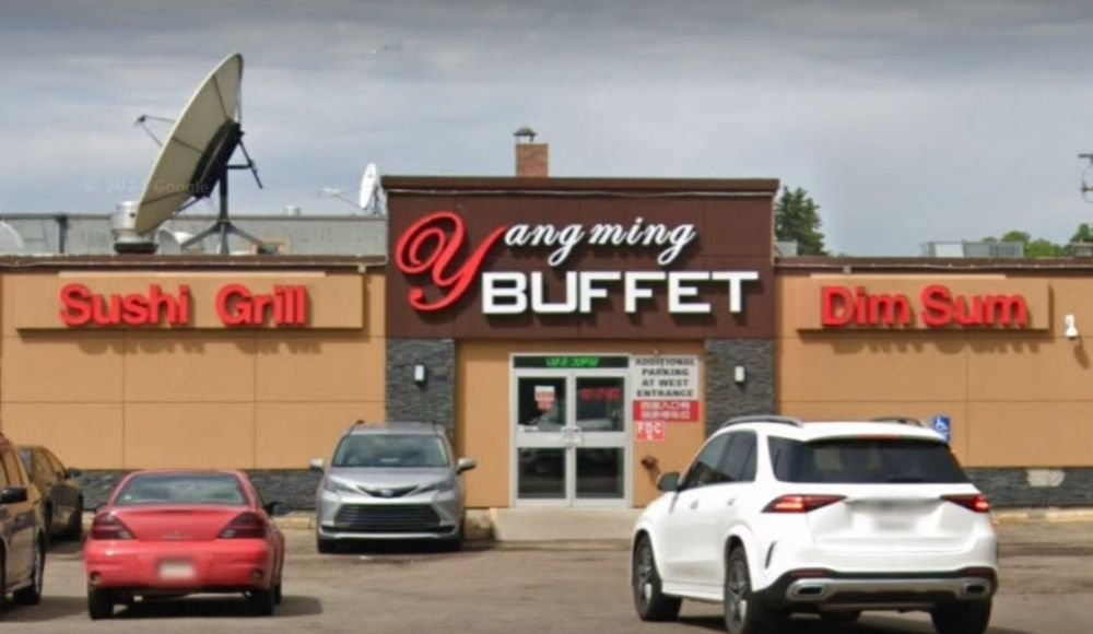 Exterior view of Yangming Buffet restaurant in Edmonton with signage for Sushi, Grill, and Dim Sum. Several cars are parked in front, highlighting its popularity among buffets in the area.