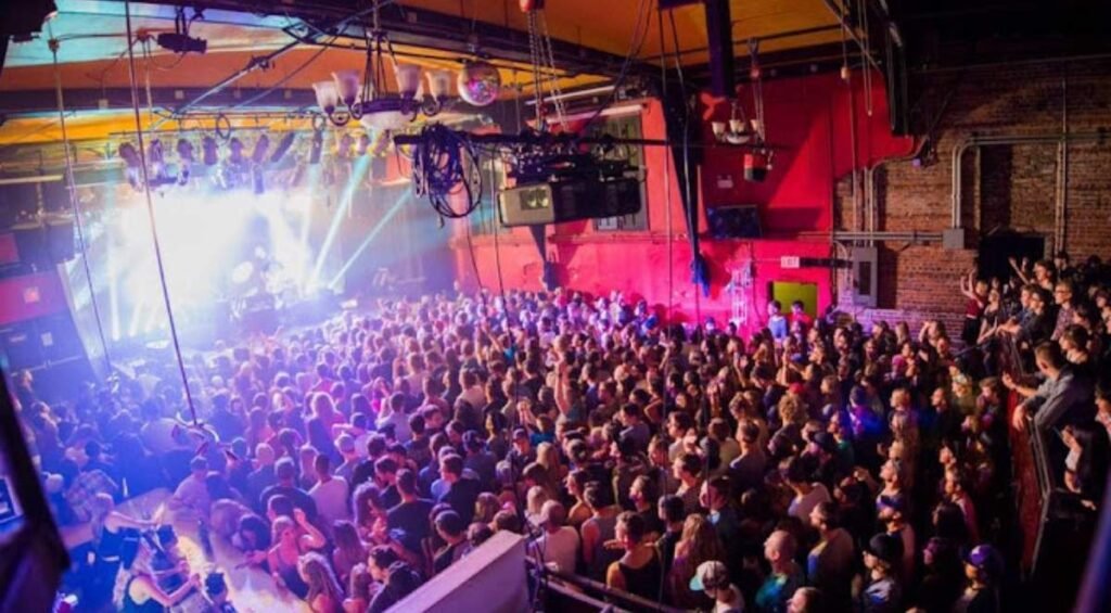 A large crowd watches live music in an Edmonton indoor venue, dimly lit with colorful stage lights.