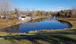 A serene bower pond surrounded by autumn trees, a boathouse, and a small dock under a clear blue sky.