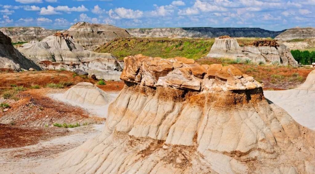 Under a partly cloudy sky, the rock formations of Dinosaur Provincial Park reveal their striking layered sediment, creating a stunning contrast against the arid landscape.