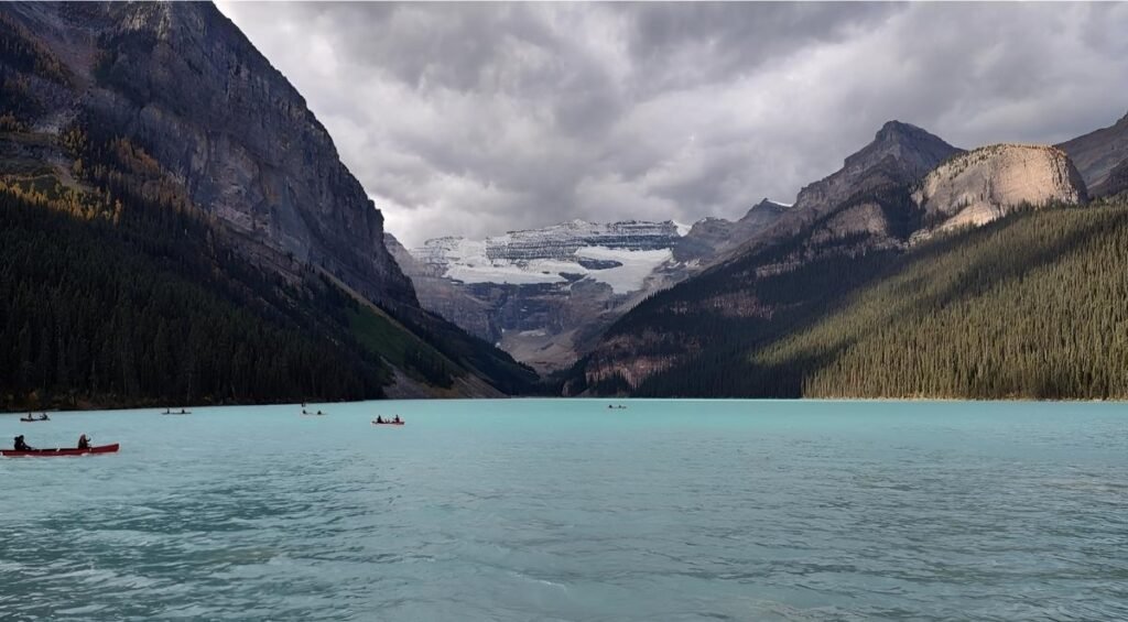 Canoes on a turquoise lake surrounded by mountains and dense forests under a cloudy sky offer a serene retreat for day trips from Calgary, providing the perfect escape into nature's embrace.