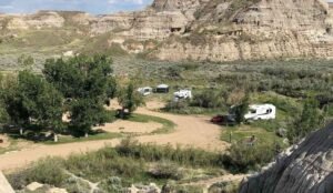 Nestled within a desert canyon, the campground at Dinosaur Provincial Park hosts RVs, tents, and vehicles. Encircled by ancient rocky hills and sparse greenery under a clear sky, this site offers campers a unique connection to the geological marvels of Alberta's badlands.