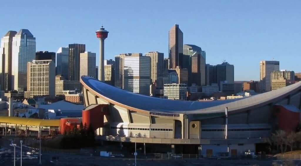 Visit Calgary to witness its stunning skyline, where modern skyscrapers tower alongside the distinctive Saddledome arena, all set against a clear blue sky.