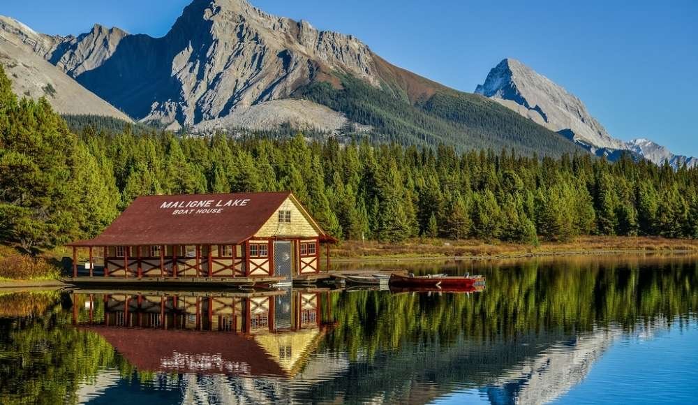 A boat house on Maligne Lake sits beside calm water, surrounded by pine trees and mountains under a clear blue sky, offering an idyllic spot for wilderness camping in Alberta's national parks.