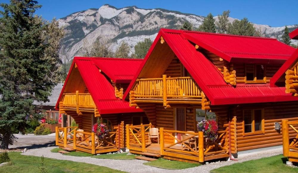 Red-roofed log cabins with balconies are set against a backdrop of trees and a mountain, offering the perfect retreat for those seeking adventure camping in Alberta's pristine wilderness.