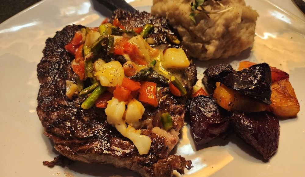 Grilled steak topped with mixed vegetables, served alongside roasted root veggies and creamy mashed potatoes—a delightful offering you'll find at restaurants in Red Deer.